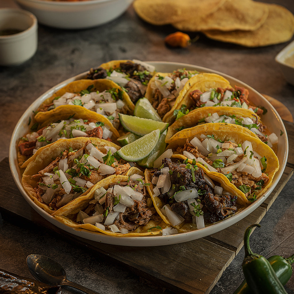 A tray filled with an assortment of tacos, with limes in the center